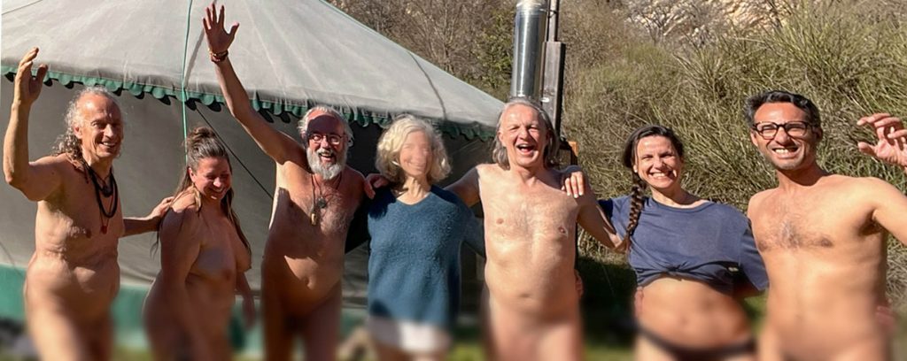 Groupe de participants en nudité bienveillante au stage La Quête de la Panthère Noire 2026, riant et célébrant joyeusement devant la yourte en pleine nature