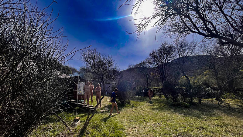 Groupe de participants au stage La Quête de la Panthère Noire 2026, nus ou en tenue légère, se détendant autour de la yourte en pleine nature ensoleillée